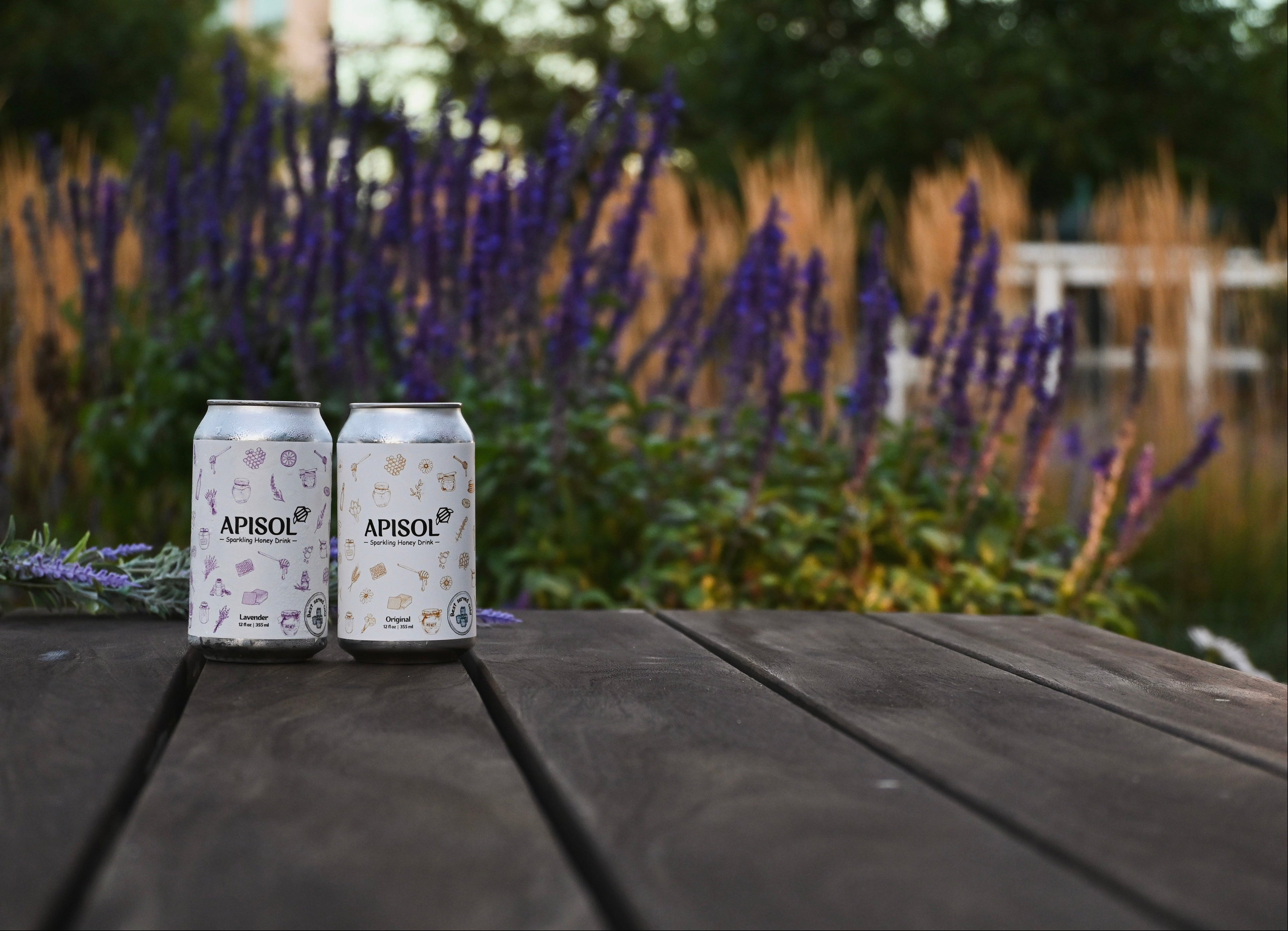 Two cans of Apisol on a wooden table with a garden background
